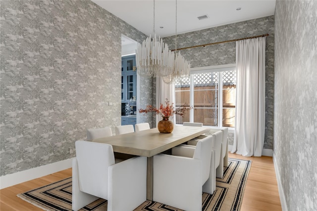 dining area featuring wallpapered walls, light wood-style floors, baseboards, and a chandelier