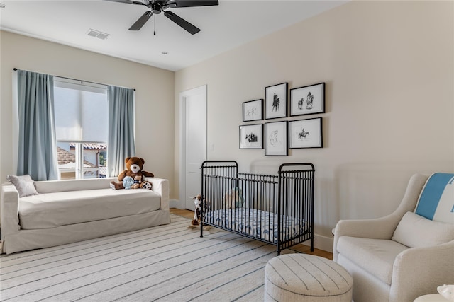 bedroom with wood finished floors, a ceiling fan, a nursery area, and baseboards
