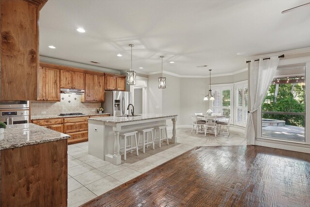 1309 Constitution Dr, Mckinney, TX 75071 - kitchen with appliances with stainless steel finishes, under cabinet range hood, backsplash, a breakfast bar, and light tile patterned floors