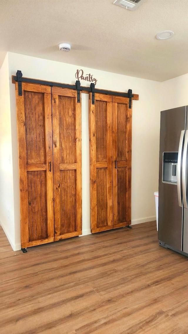1709 Pamela Ln, Fort Worth, TX 76112 - kitchen featuring stainless steel refrigerator with ice dispenser, light wood finished floors, a barn door, and baseboards