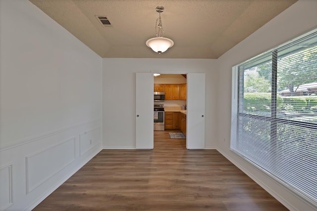 unfurnished dining area featuring dark wood-style floors, a textured ceiling, and baseboards