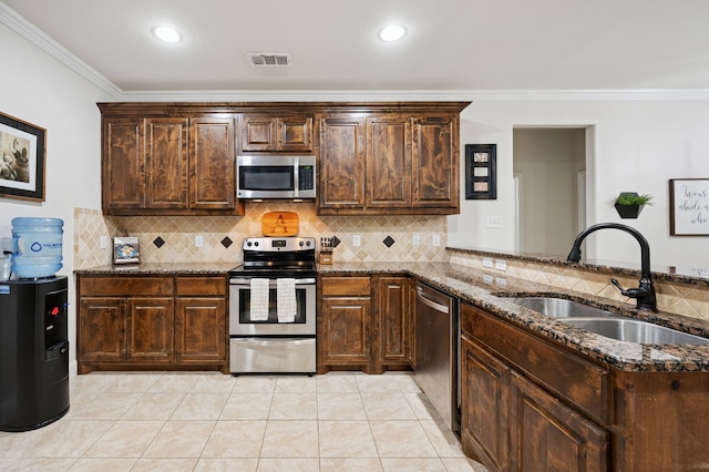 kitchen featuring appliances with stainless steel finishes, a sink, dark stone counters, crown molding, and dark brown cabinets