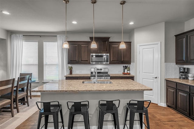 411 Skipper Ln, Azle, TX 76020 - kitchen featuring stainless steel appliances, a sink, decorative backsplash, dark brown cabinets, and a breakfast bar area