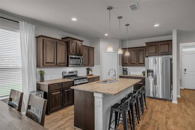411 Skipper Ln, Azle, TX 76020 - kitchen featuring appliances with stainless steel finishes, a sink, dark brown cabinetry, a kitchen breakfast bar, and light wood-style flooring