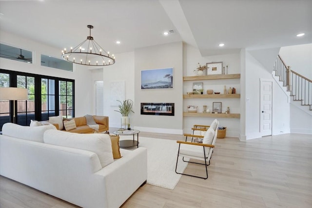 living room featuring light wood finished floors, recessed lighting, a glass covered fireplace, stairs, and a chandelier