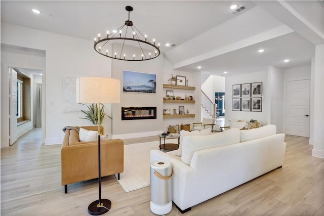 living area with stairway, a chandelier, a glass covered fireplace, light wood-style floors, and recessed lighting