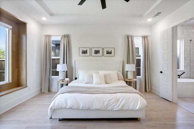 bedroom featuring multiple windows, light wood-style floors, a tray ceiling, and recessed lighting