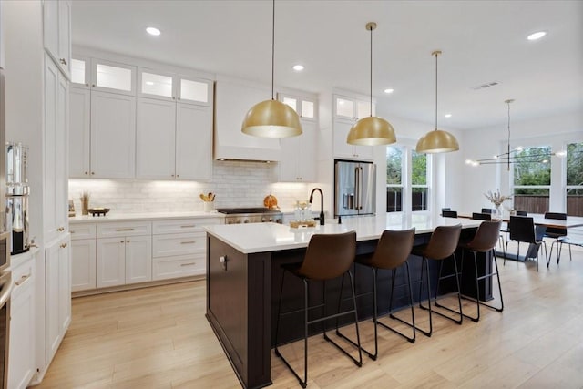 kitchen with high quality fridge, tasteful backsplash, an island with sink, light countertops, and light wood-type flooring
