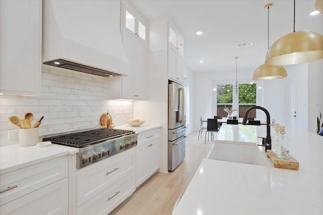 kitchen featuring premium range hood, stainless steel appliances, white cabinetry, light countertops, and backsplash