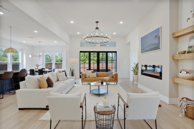 living room featuring a chandelier, light wood-style floors, recessed lighting, and a glass covered fireplace