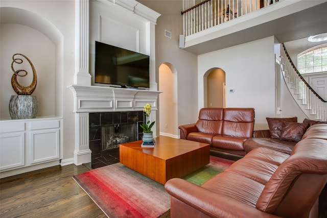 6513 Crawley Dr, Plano, TX 75093 - living room with arched walkways, dark wood finished floors, a towering ceiling, stairs, and a tiled fireplace