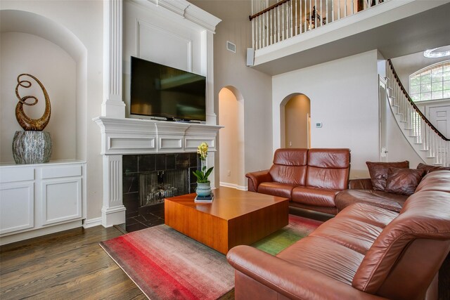 6513 Crawley Dr, Plano, TX 75093 - living room with arched walkways, dark wood finished floors, a towering ceiling, stairs, and a tiled fireplace