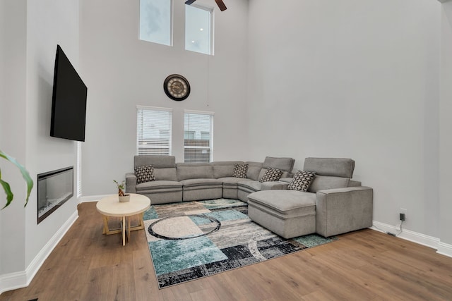 4533 Wilbarger St, Plano, TX 75024 - living room with baseboards, wood finished floors, a high ceiling, ceiling fan, and a glass covered fireplace