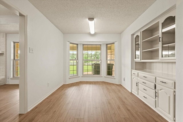 unfurnished dining area featuring light wood-style flooring, a textured ceiling, and baseboards
