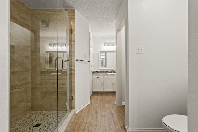 full bathroom featuring wood finished floors, a stall shower, vanity, a textured ceiling, and toilet