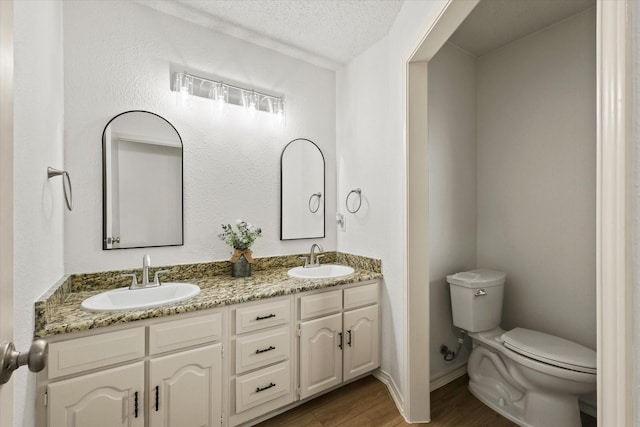 full bathroom with toilet, wood finished floors, double vanity, baseboards, and a textured ceiling