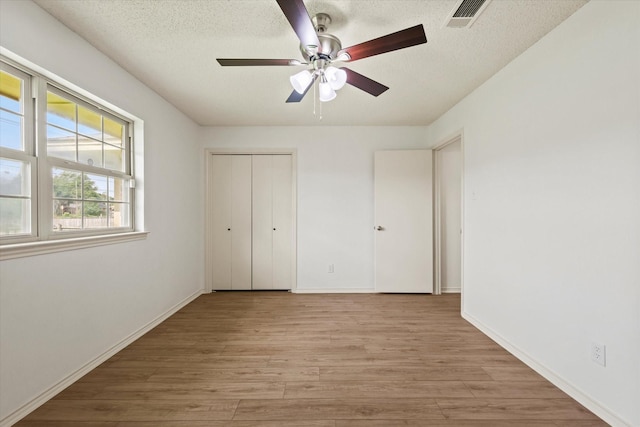 unfurnished bedroom featuring light wood finished floors, a textured ceiling, a closet, baseboards, and ceiling fan