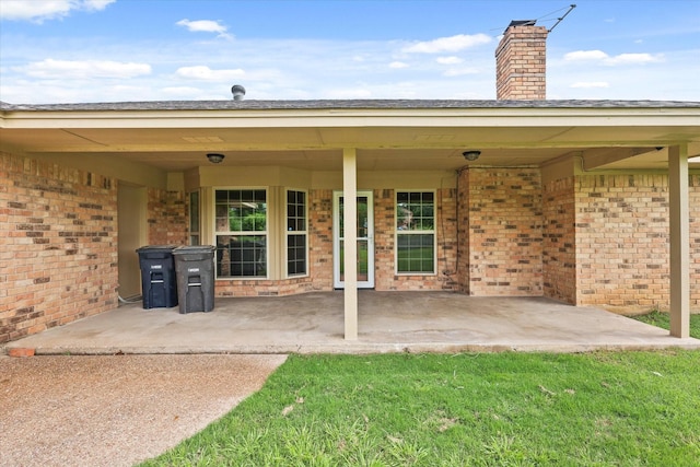 rear view of property with brick siding, a chimney, and a patio