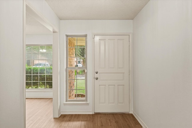doorway to outside with wood finished floors, a textured ceiling, and baseboards