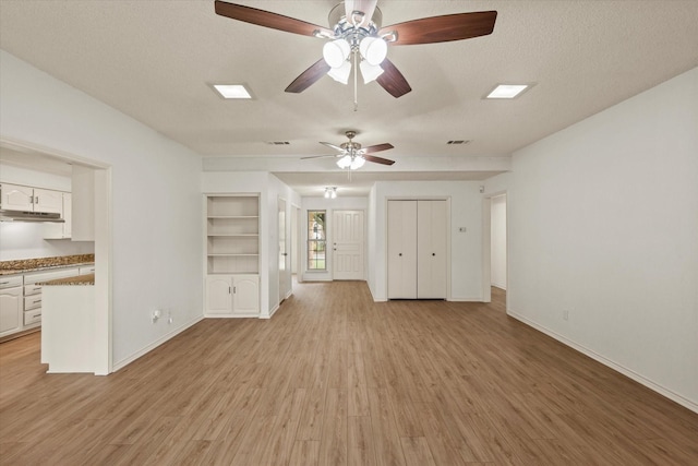 unfurnished living room with ceiling fan, light wood-style flooring, baseboards, a textured ceiling, and built in features