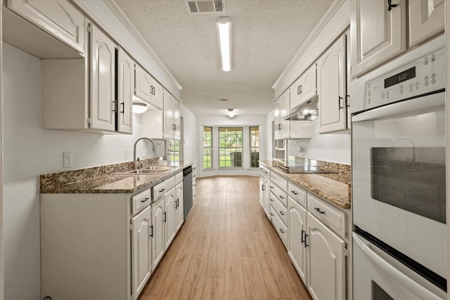 kitchen with a sink, a textured ceiling, stainless steel dishwasher, light wood finished floors, and double oven