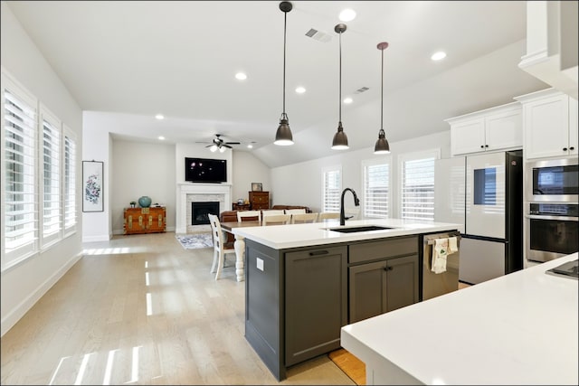 8529 Melrose, The Colony, TX 75056 - kitchen with a sink, stainless steel appliances, a fireplace, light wood finished floors, and white cabinetry