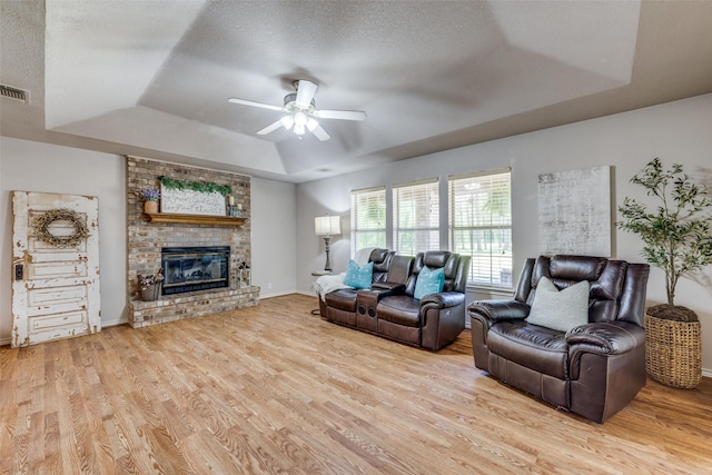 4942 US Highway 69, Denison, TX 75021 - living area featuring a tray ceiling, a ceiling fan, light wood-type flooring, a brick fireplace, and a textured ceiling