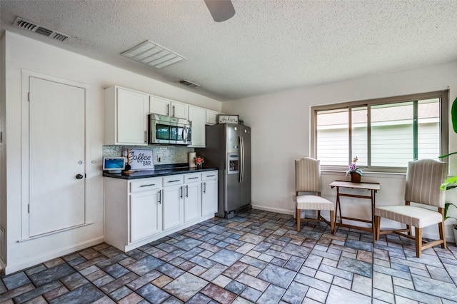 kitchen with stainless steel appliances, a textured ceiling, white cabinets, dark countertops, and backsplash