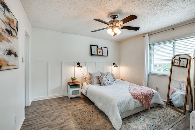 bedroom with a decorative wall, wood finished floors, a wainscoted wall, a textured ceiling, and ceiling fan