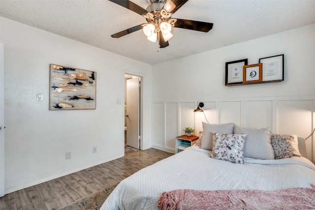 bedroom featuring wood finished floors, a ceiling fan, a decorative wall, and wainscoting