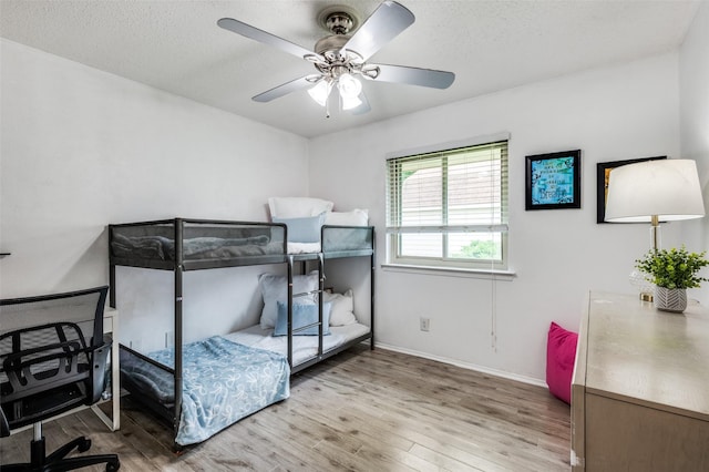 bedroom featuring wood finished floors, baseboards, a ceiling fan, a textured ceiling, and an office area