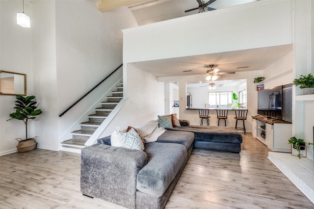 living room with light wood-style floors, a ceiling fan, stairs, a high ceiling, and baseboards