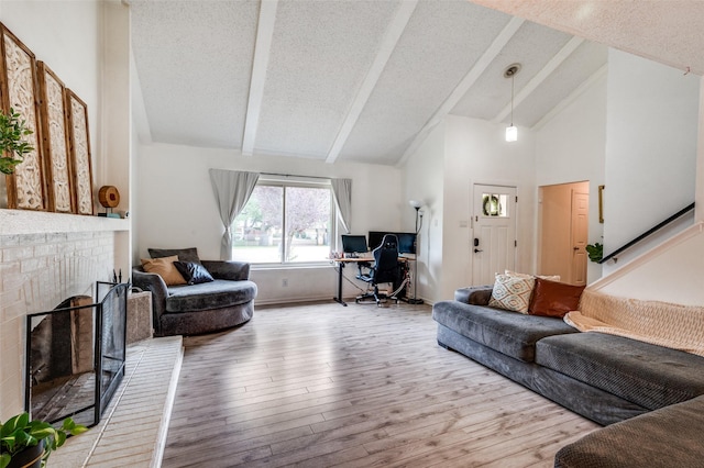 living room with beamed ceiling, wood finished floors, high vaulted ceiling, a textured ceiling, and a brick fireplace