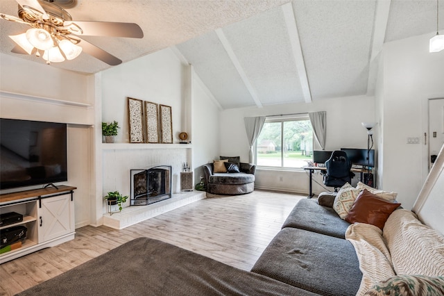 living area featuring light wood-style floors, ceiling fan, a fireplace, and a textured ceiling