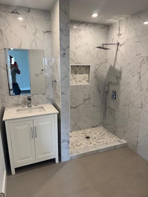 bathroom with a marble finish shower, vanity, and tile walls