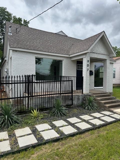 view of front of home featuring a shingled roof, brick siding, and fence