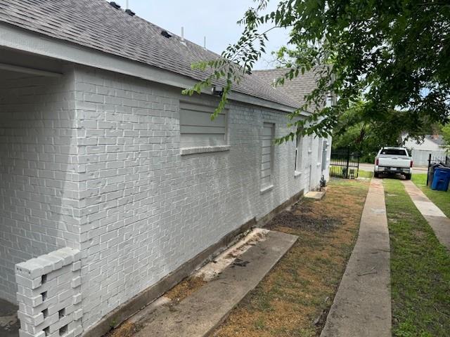 view of property exterior with a shingled roof, brick siding, and fence