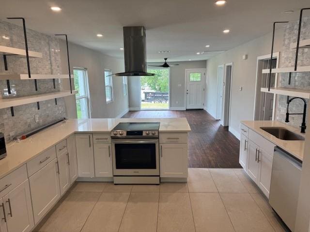 kitchen featuring appliances with stainless steel finishes, island exhaust hood, a sink, a peninsula, and light countertops