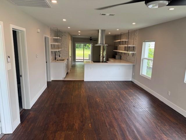 kitchen featuring exhaust hood, light countertops, wood finished floors, a peninsula, and baseboards