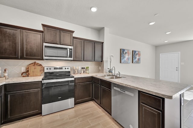 2867 Baneberry Ln, Mesquite, TX 75150 - kitchen with appliances with stainless steel finishes, a peninsula, tasteful backsplash, dark brown cabinets, and light countertops