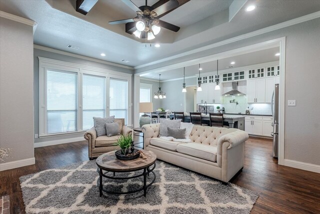 living room with baseboards, a ceiling fan, ornamental molding, dark wood finished floors, and a chandelier