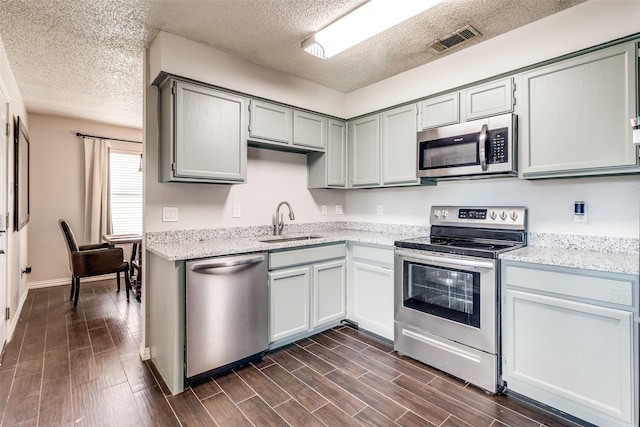2802 Rio Grande Pass, Mesquite, TX 75150 - kitchen featuring appliances with stainless steel finishes, a sink, a textured ceiling, gray cabinetry, and dark wood-type flooring