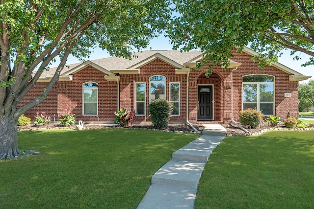 view of front facade with brick siding, a front yard, and a shingled roof