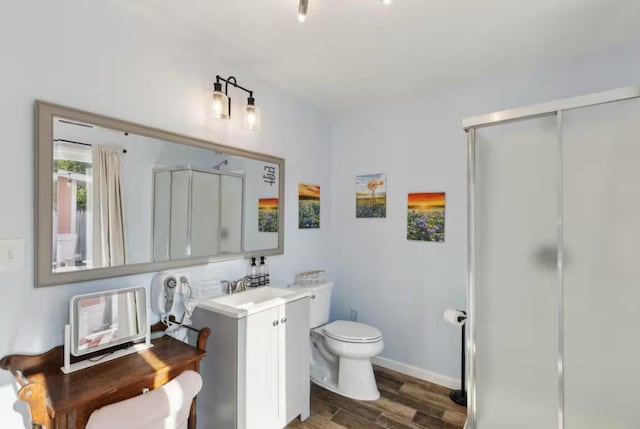 bathroom featuring toilet, a stall shower, wood finished floors, vanity, and baseboards