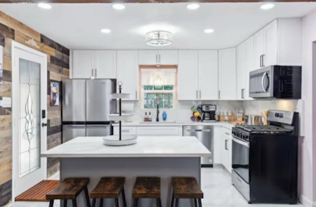 kitchen featuring appliances with stainless steel finishes, a sink, a kitchen bar, light countertops, and recessed lighting