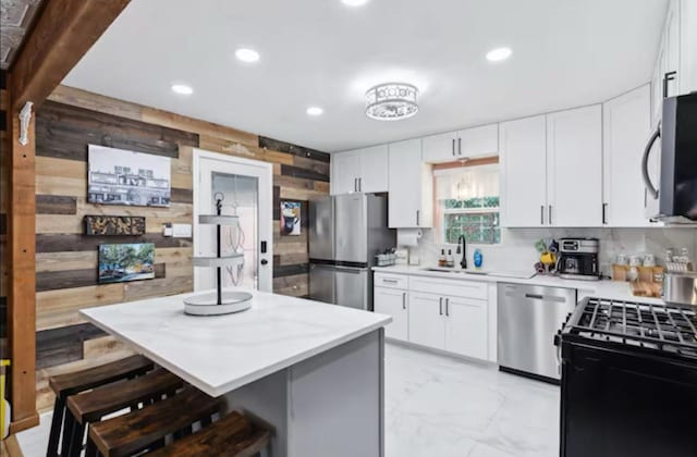 kitchen with stainless steel appliances, a sink, wood walls, light marble finish flooring, and a breakfast bar area