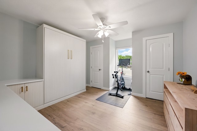 workout room featuring light wood-style flooring, a ceiling fan, and baseboards