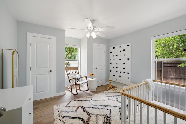 bedroom featuring wood finished floors, a nursery area, baseboards, and ceiling fan