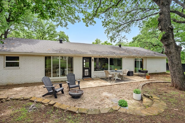 rear view of property featuring brick siding, an outdoor fire pit, a patio, and roof with shingles