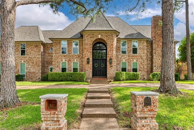 view of front of property featuring brick siding, a shingled roof, a chimney, and a front lawn